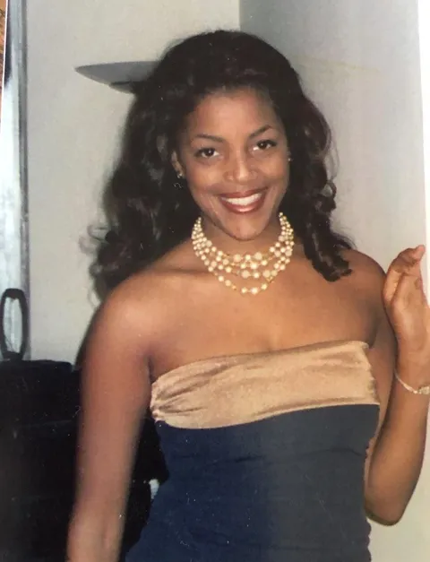 Tami in graduate school, smiling in a strapless top and pearl necklace